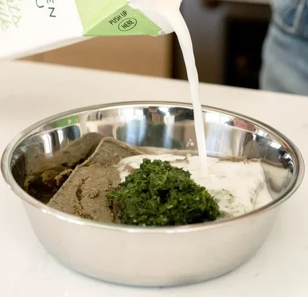 Dog food topper and greens being added to a bowl